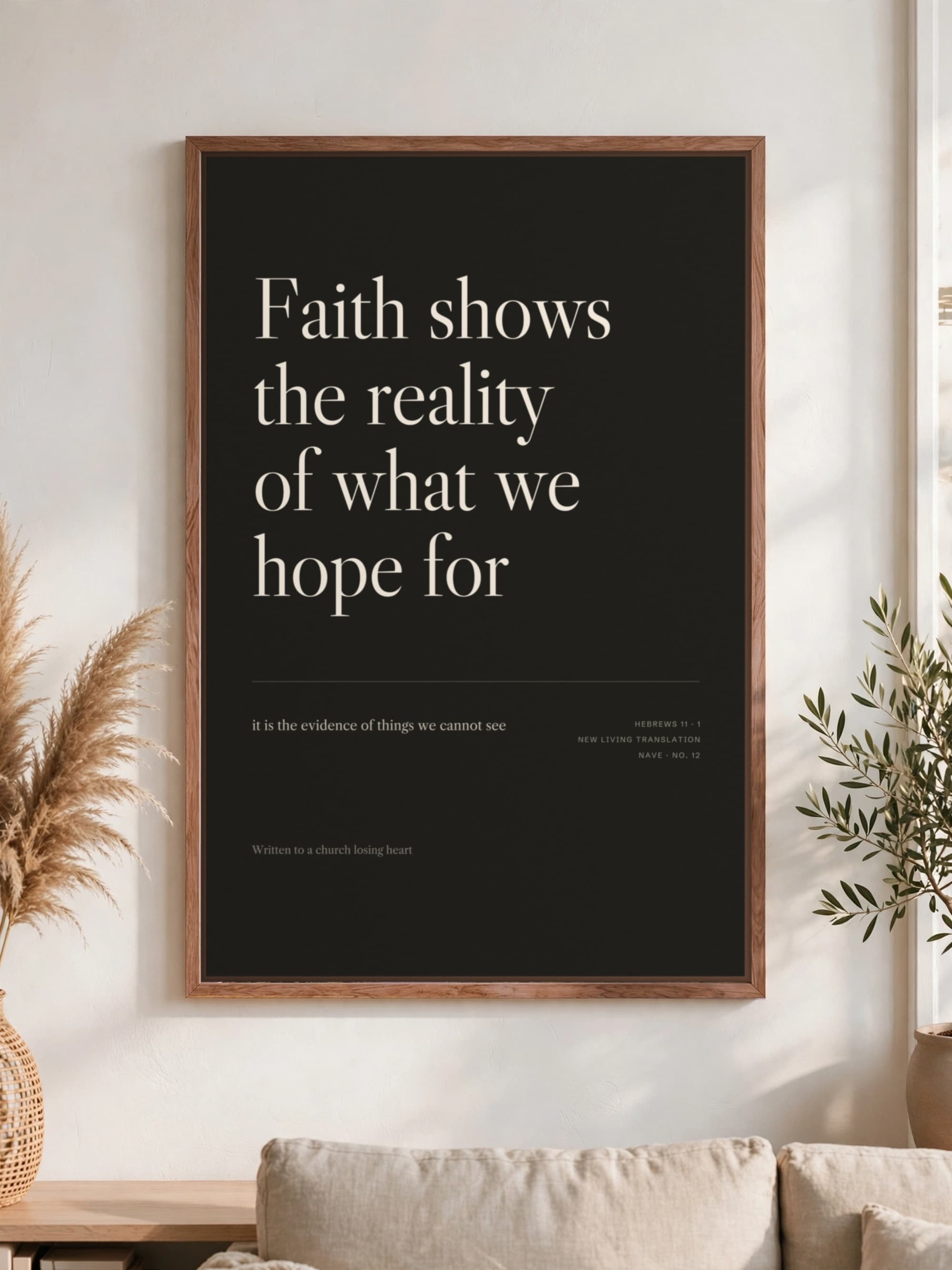 “Faith shows the reality of what we hope for” in cream serif on near-black, pecan frame, hung above a linen sofa.