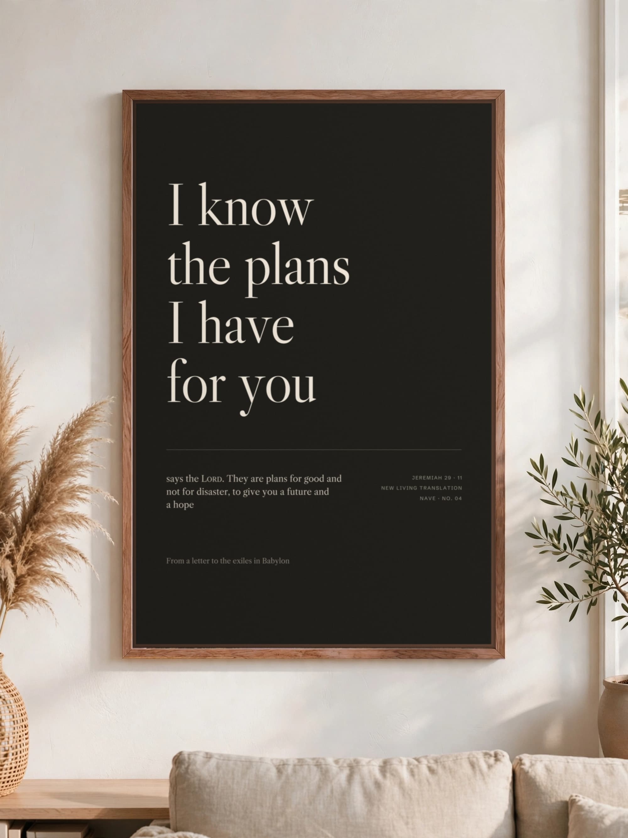 “I know the plans I have for you” in cream serif on near-black canvas, pecan frame, hung above a linen sofa.