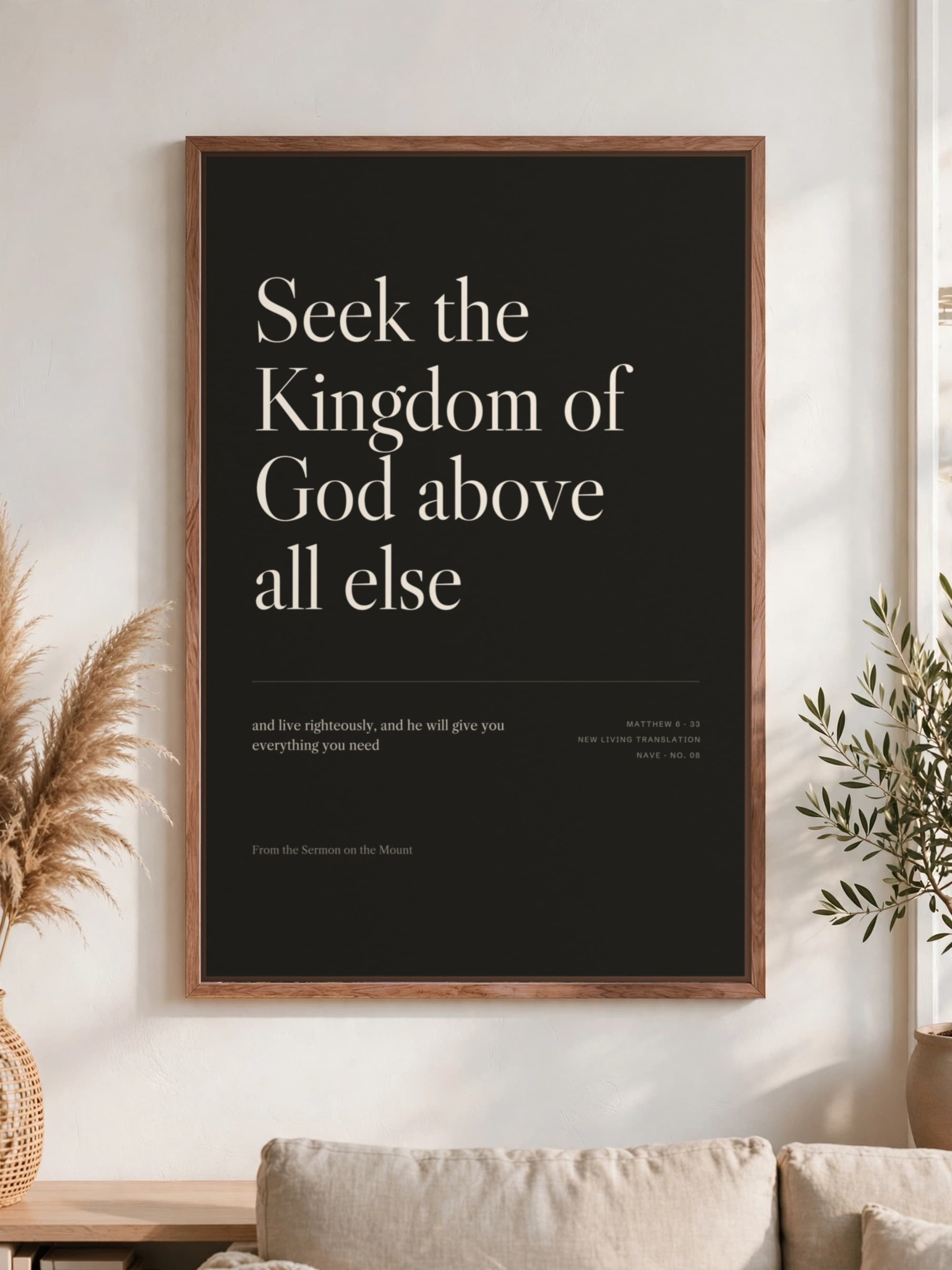 “Seek the Kingdom of God above all else” in cream serif on near-black canvas, pecan frame, hung above a linen sofa.