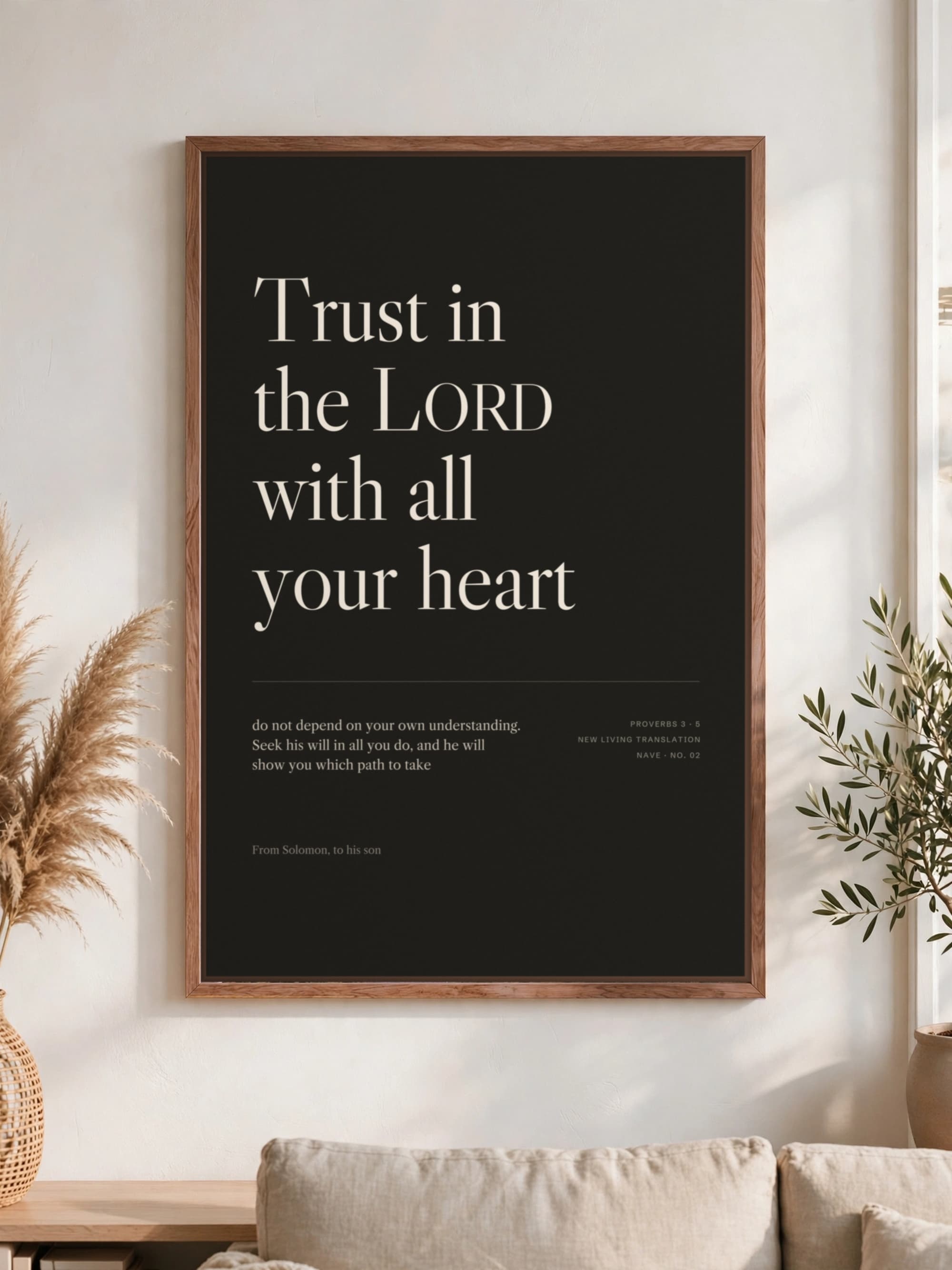 “Trust in the LORD with all your heart” in cream serif on near-black canvas, pecan frame, hung above a linen sofa.