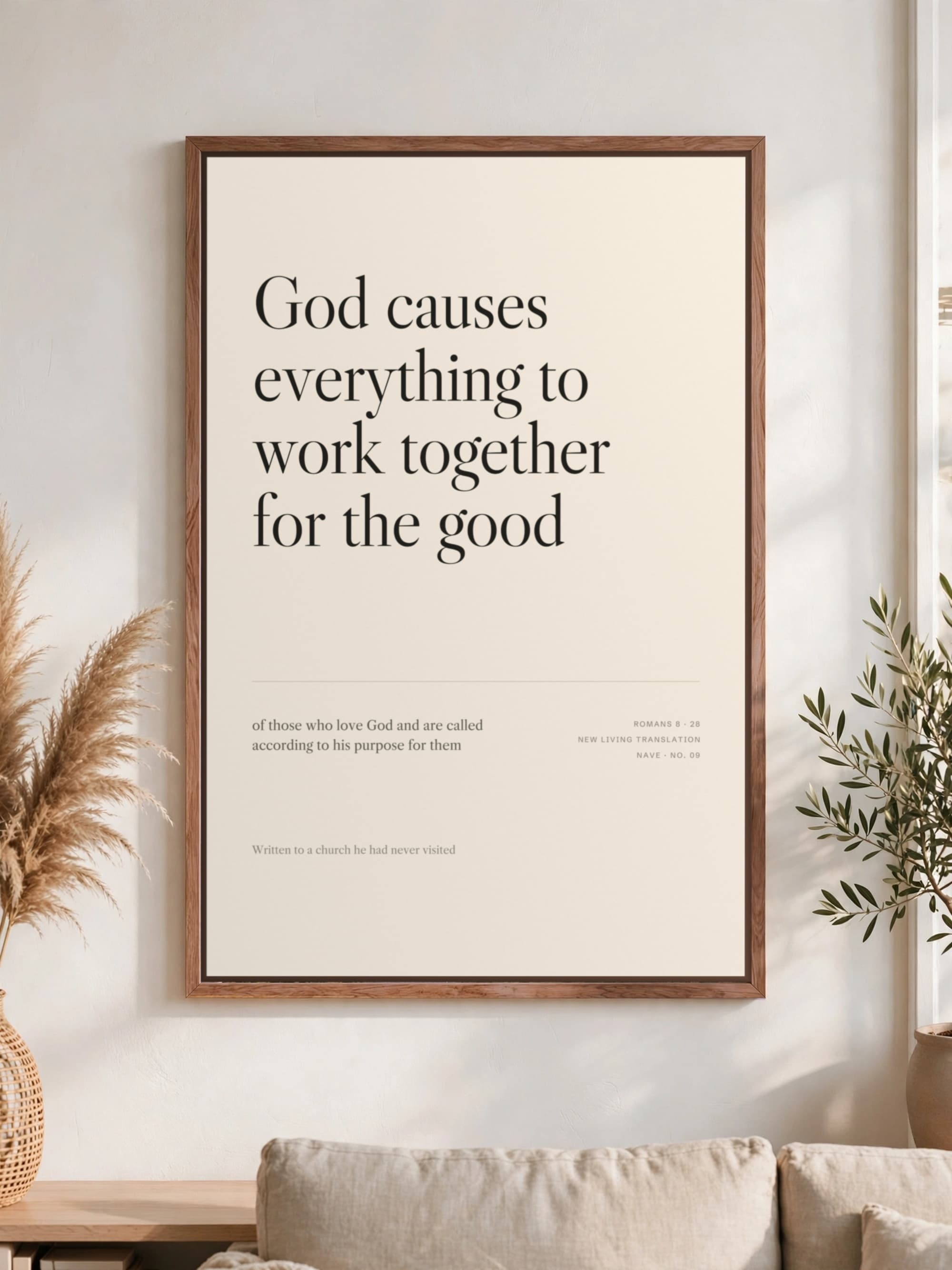 “God causes everything to work together for the good” in dark serif on cream, pecan frame, hung above a linen sofa.