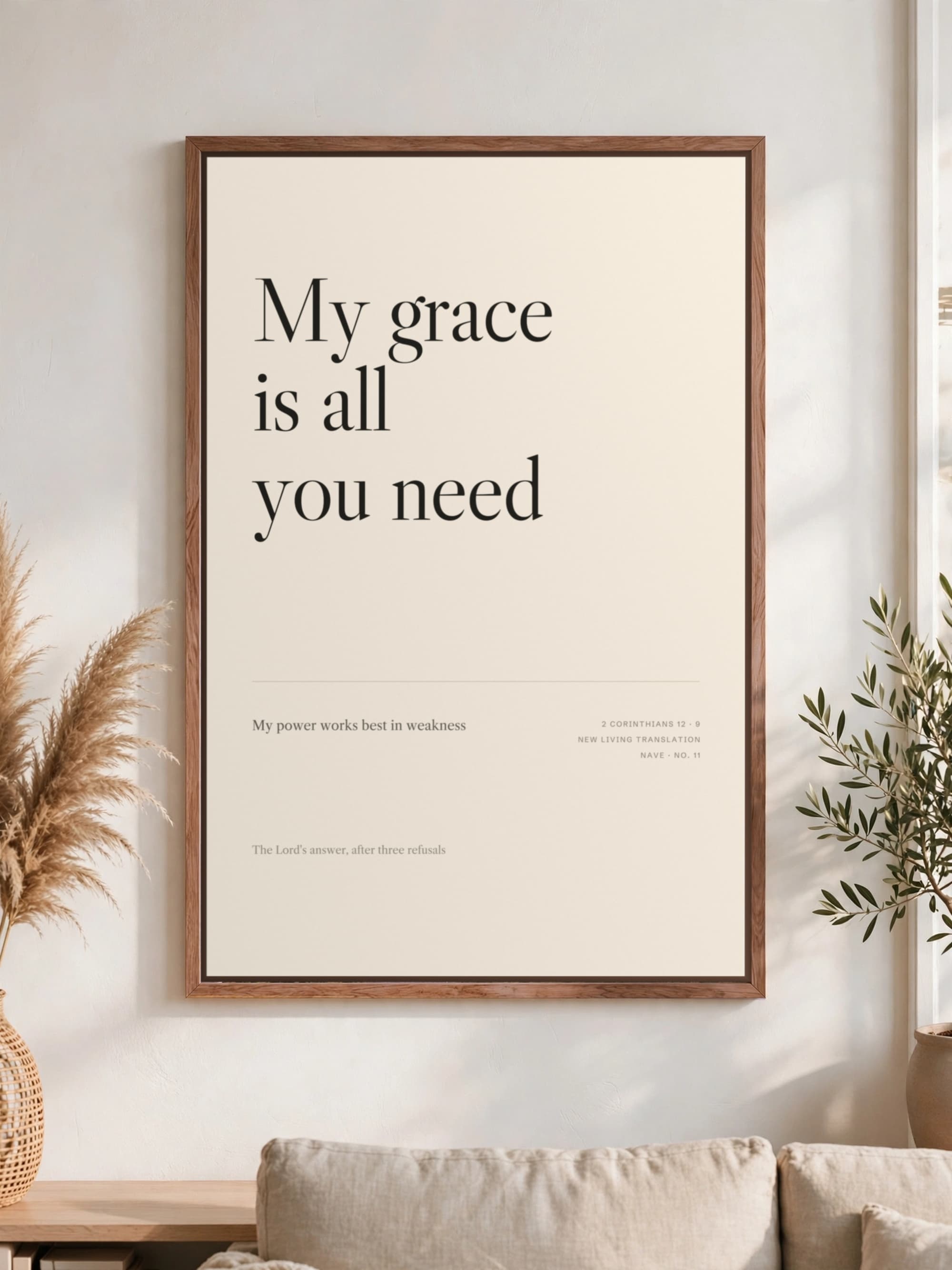 “My grace is all you need” in dark serif on cream canvas, pecan frame, hung above a linen sofa.