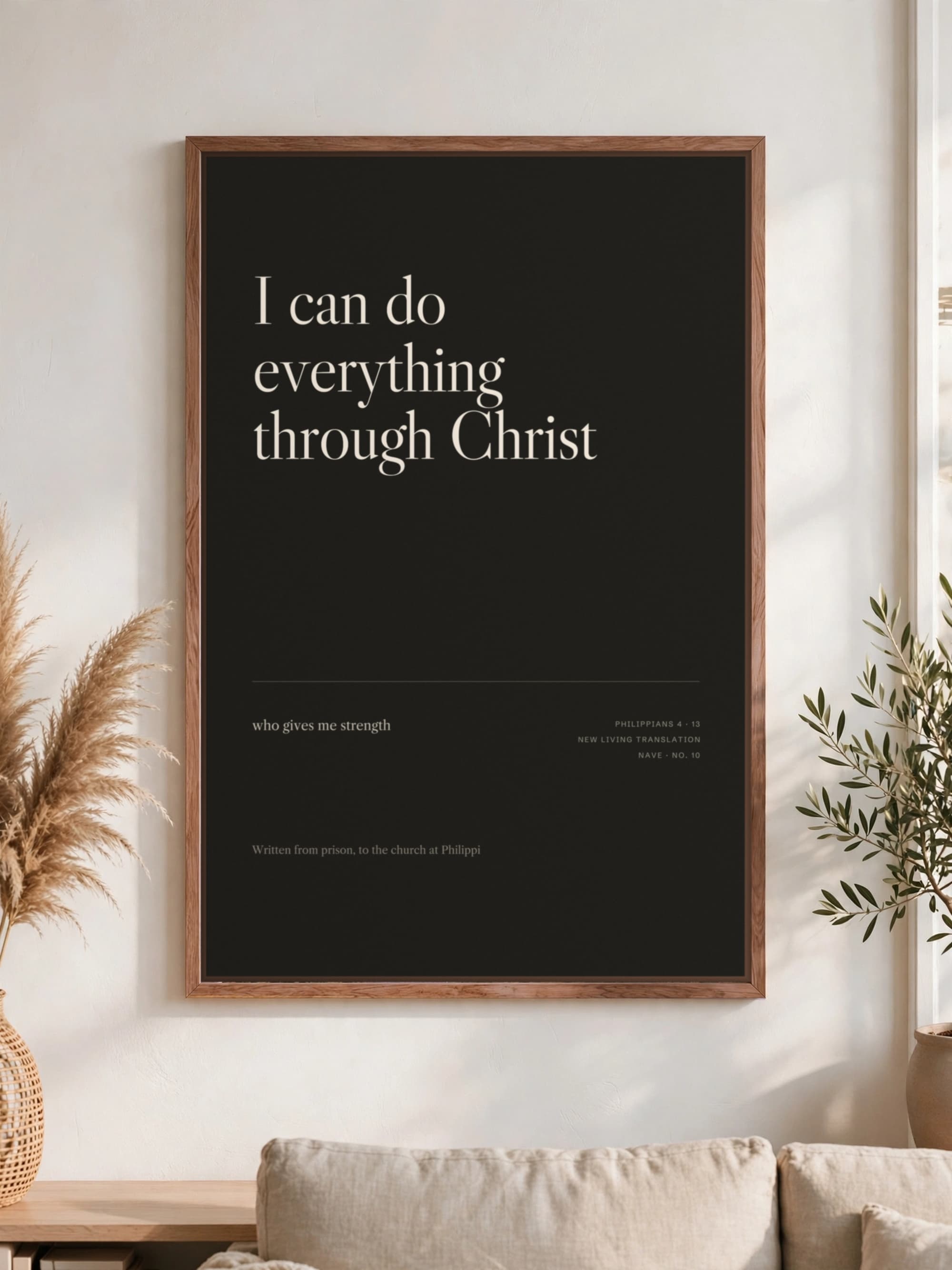 “I can do everything through Christ” in cream serif on near-black canvas, pecan frame, hung above a linen sofa.
